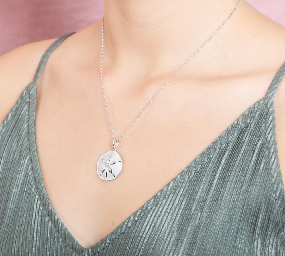 The picture shows a model wearing a white gold sand dollar pendant with topaz.