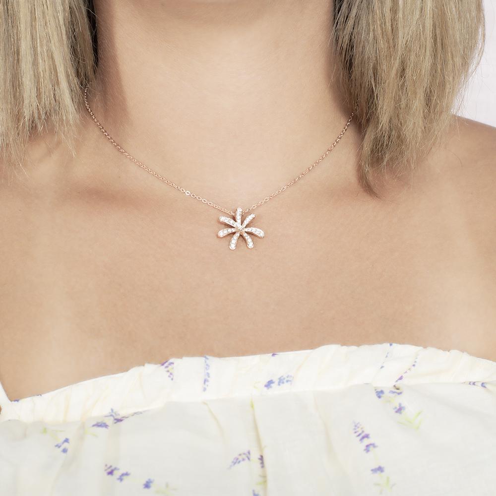 In this photo there is a model with blonde hair and a white shirt with purple flowers, wearing a rose gold tiare gardenia pendant with topaz gemstones.