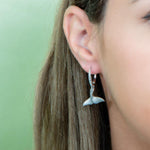 The picture shows a model wearing a 925 sterling silver whale tail earring with topaz.